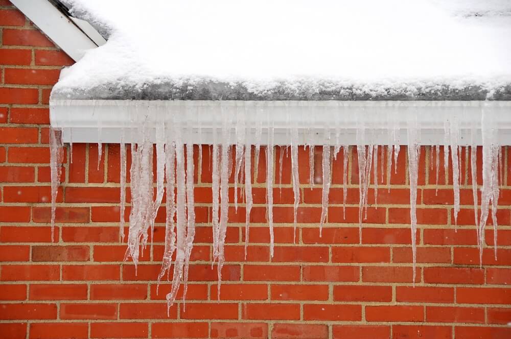 brick house with ice dams and snow on roof/gutters